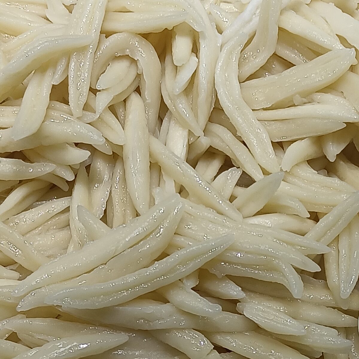 A close-up heap of pale, hand-cut maoerduo dough pieces, small curled strips of pasta
