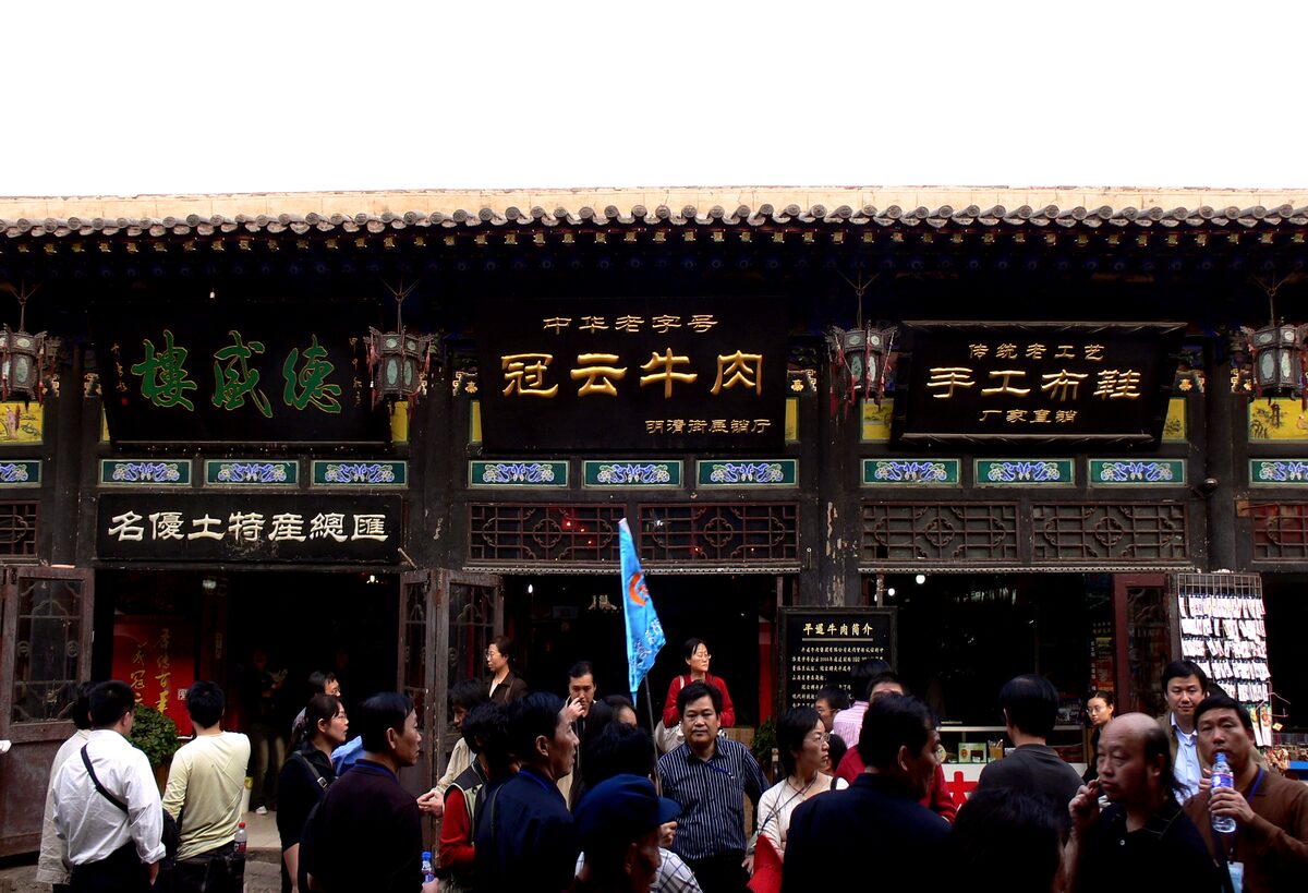 The dark wooden shopfront of a Pingyao beef shop with gold signboards, with a crowd of visitors outside