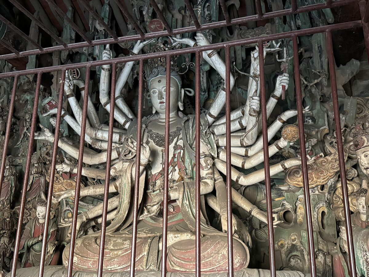 The painted clay 26-armed Guanyin in the Bodhisattva Hall at Shuanglin Temple, seen through an iron grille