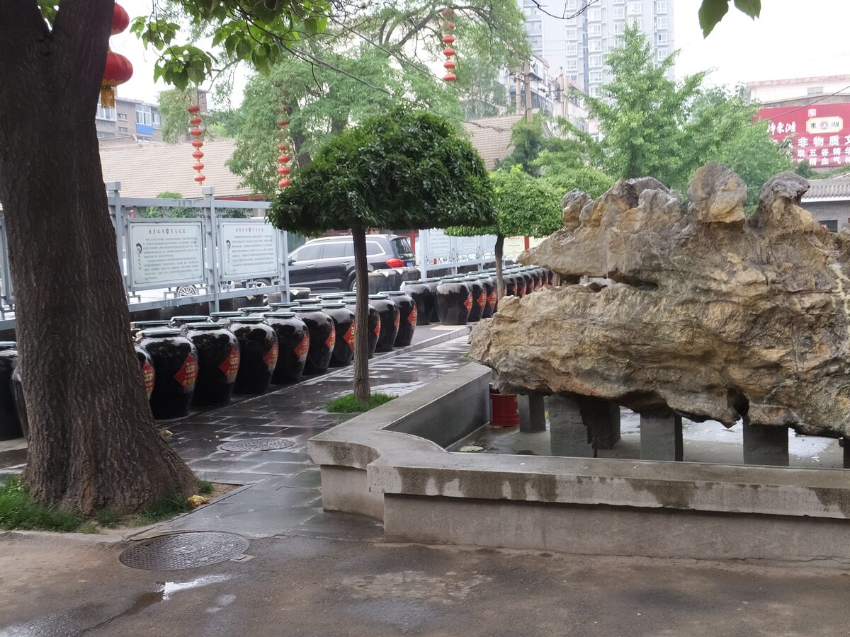 Rows of black clay vinegar jars standing in a courtyard beside a rock garden at the Donghu vinegar works in Taiyuan