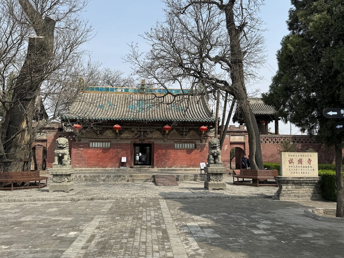 The red-walled Heavenly Kings Hall of Zhenguo Temple with stone lions at the door and bare trees in the courtyard