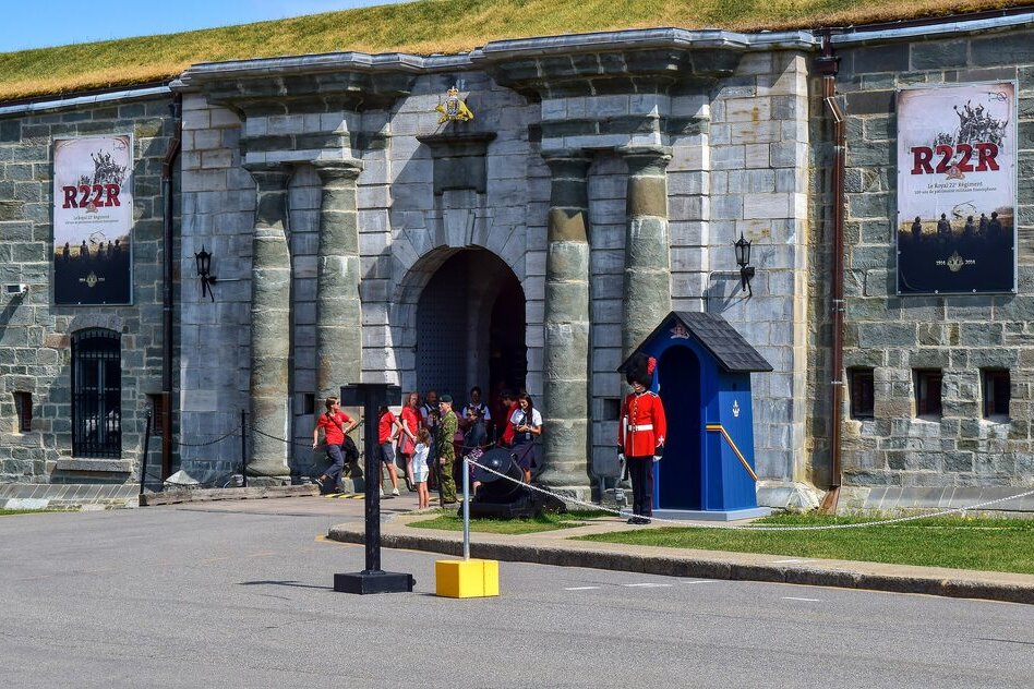 The stone gate of the Citadelle of Quebec with a guard in red tunic and bearskin hat beside his blue sentry box