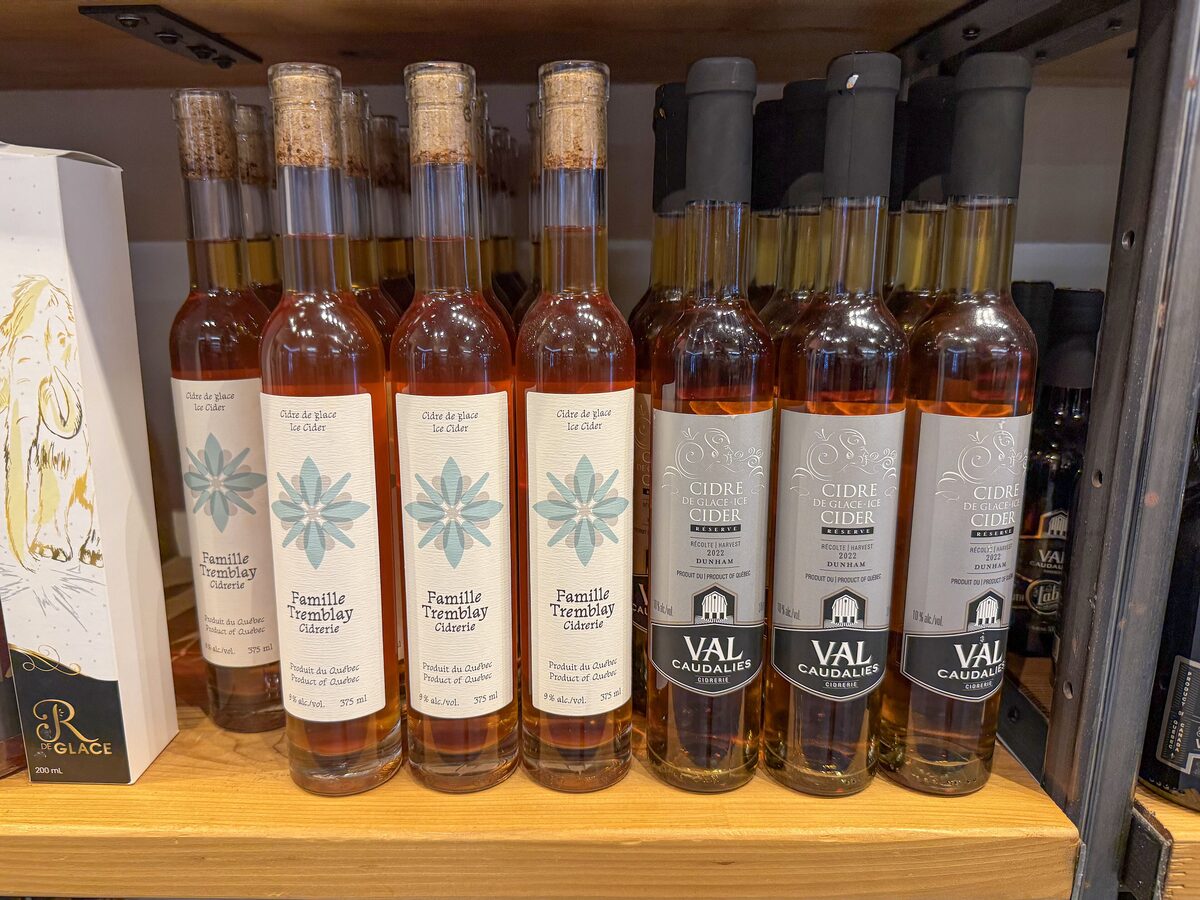 Two rows of slim ice cider bottles from Quebec cideries on a wooden shop shelf