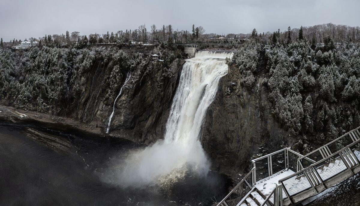 Montmorency Falls plunging into the gorge in early winter, with frosted trees, a stair viewing platform and the footbridge across the top