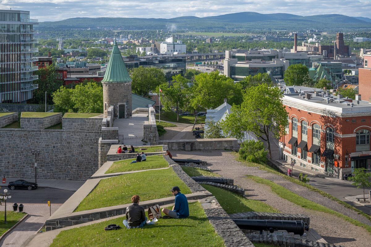 The grassy stone ramparts of Old Quebec with a corner tower and cannons, and the city and distant hills beyond