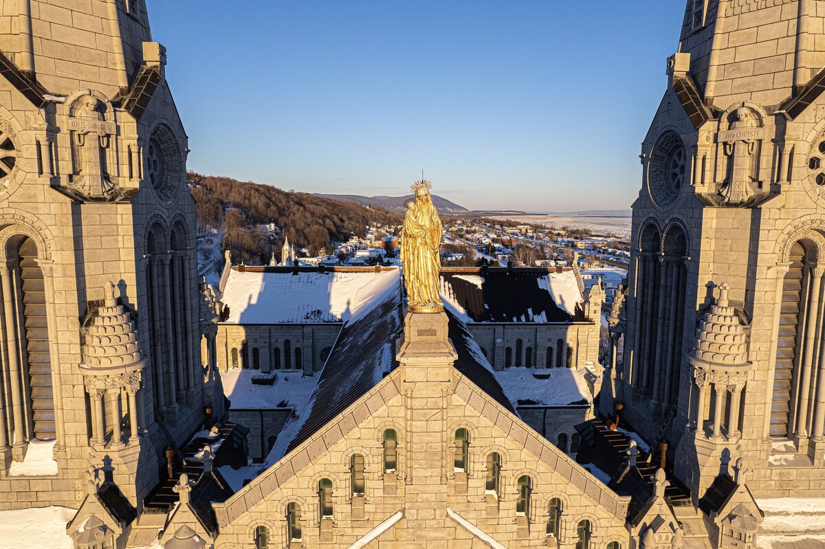 The twin spires of the Sainte-Anne-de-Beaupré basilica with the golden statue of Saint Anne and snow on the roofs