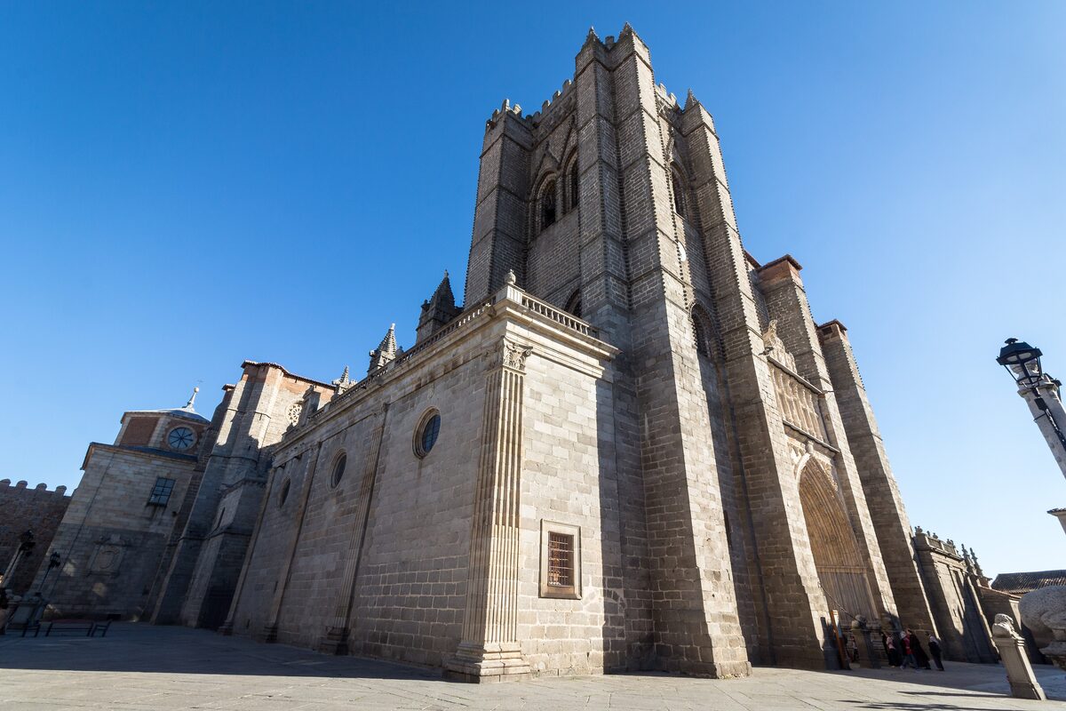The tall granite flank of Ávila Cathedral with its plain tower under a blue sky