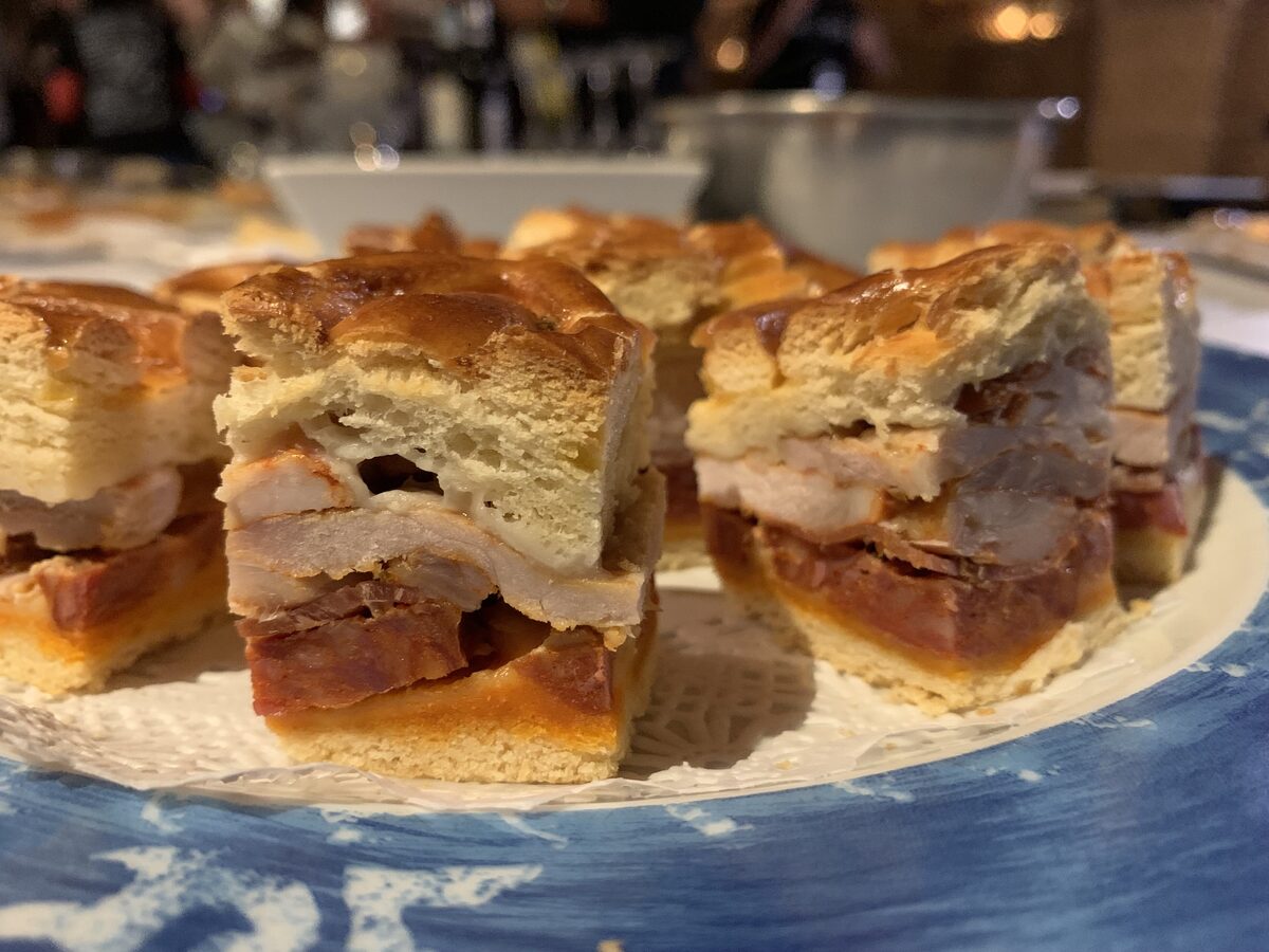 Cut squares of hornazo on a plate, a golden bread crust around layers of pork loin and chorizo