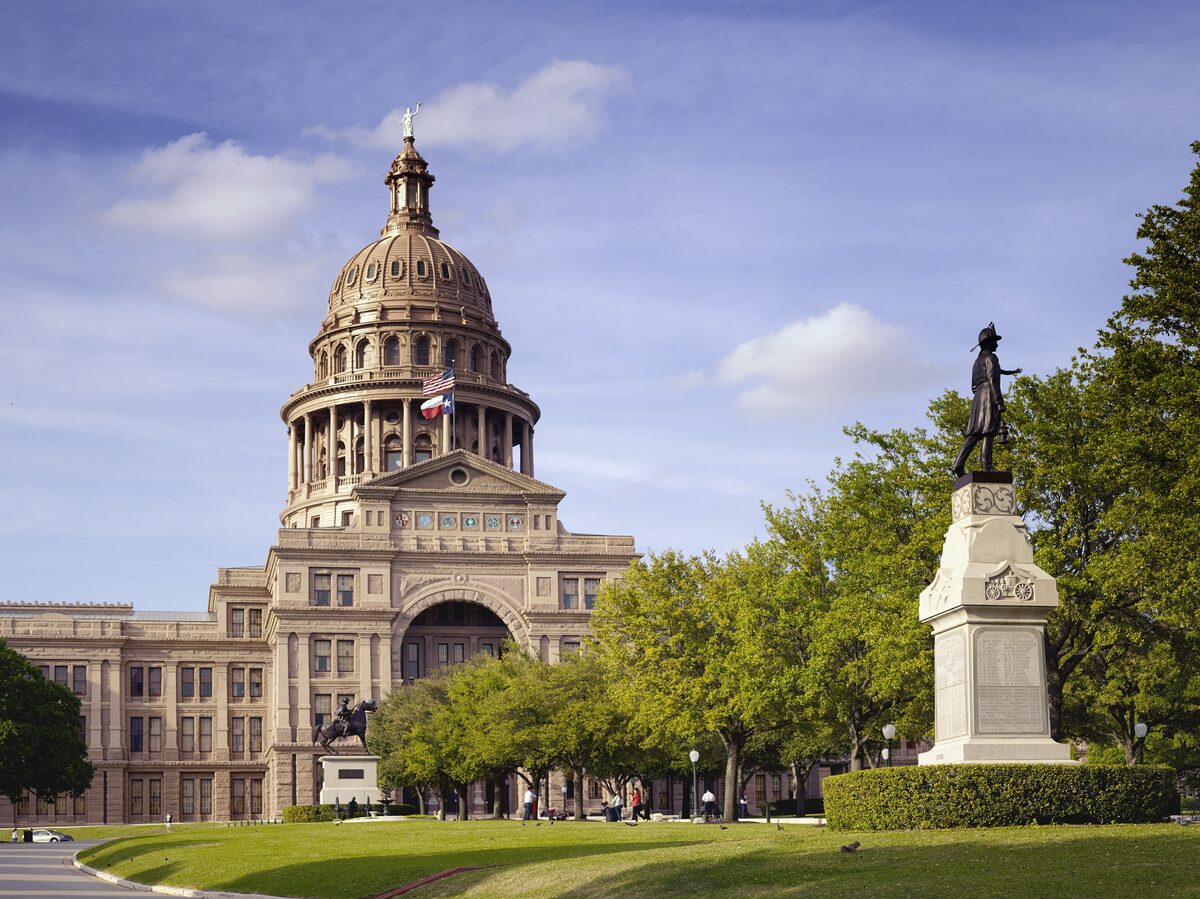 The pink granite Texas State Capitol dome in Austin with a statue on the lawn in front
