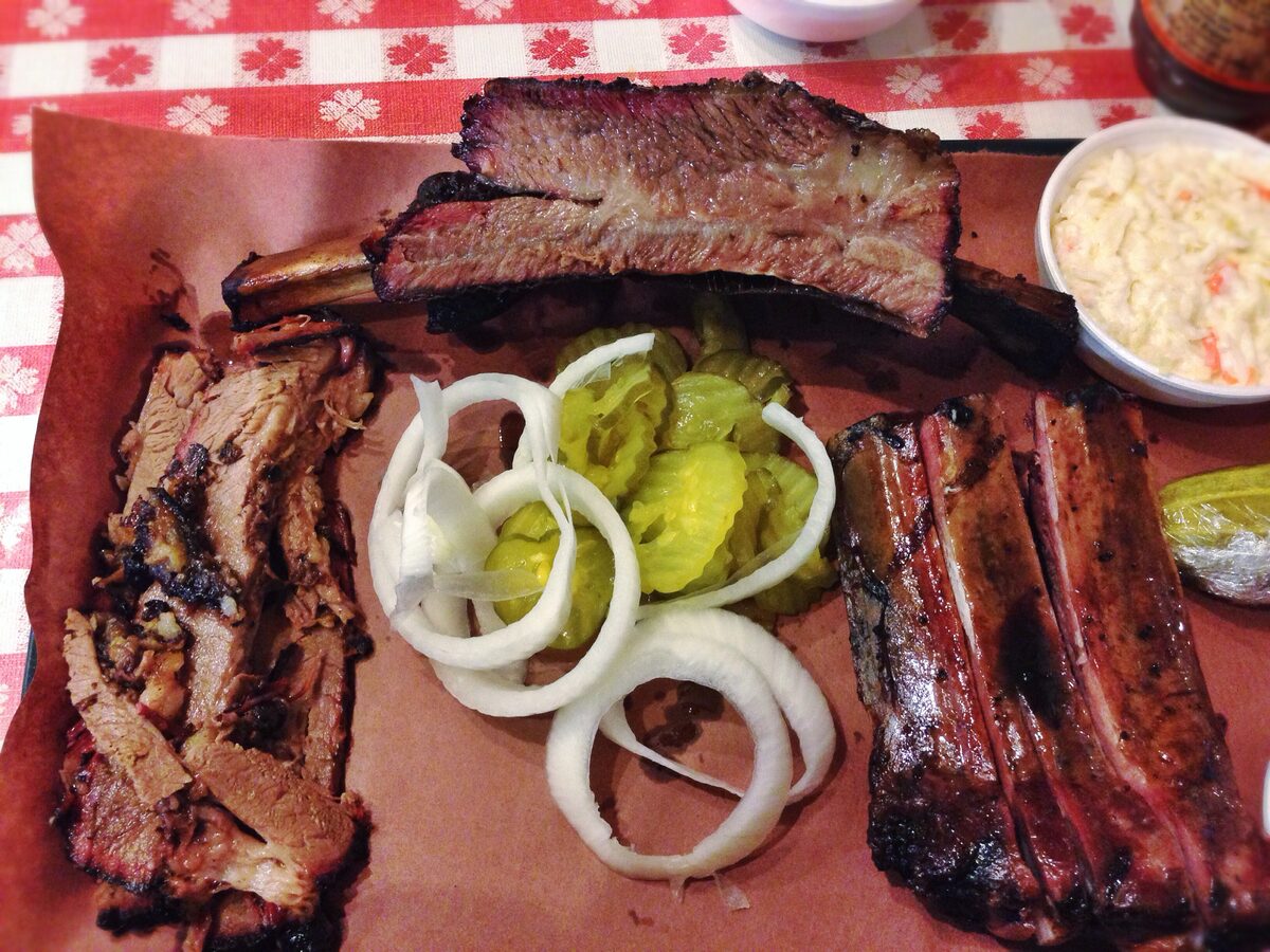 Texas barbecue on butcher paper: sliced brisket, a beef rib, pickles and onion