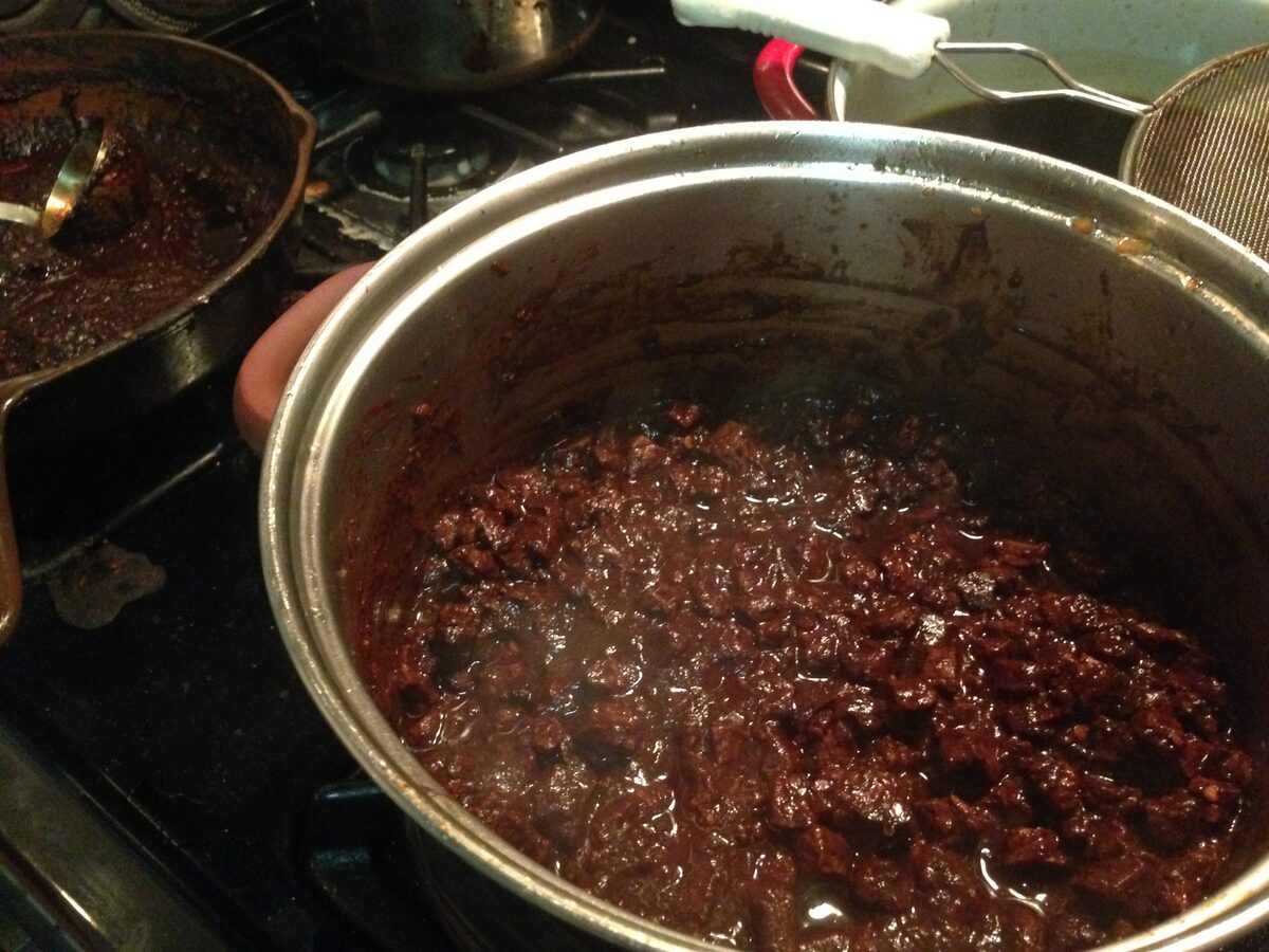 A pot of dark, bean-free chili con carne simmering on a stove