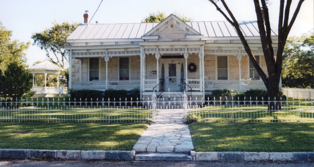 A Victorian cottage with a lacy porch, picket fence and metal roof in Fredericksburg