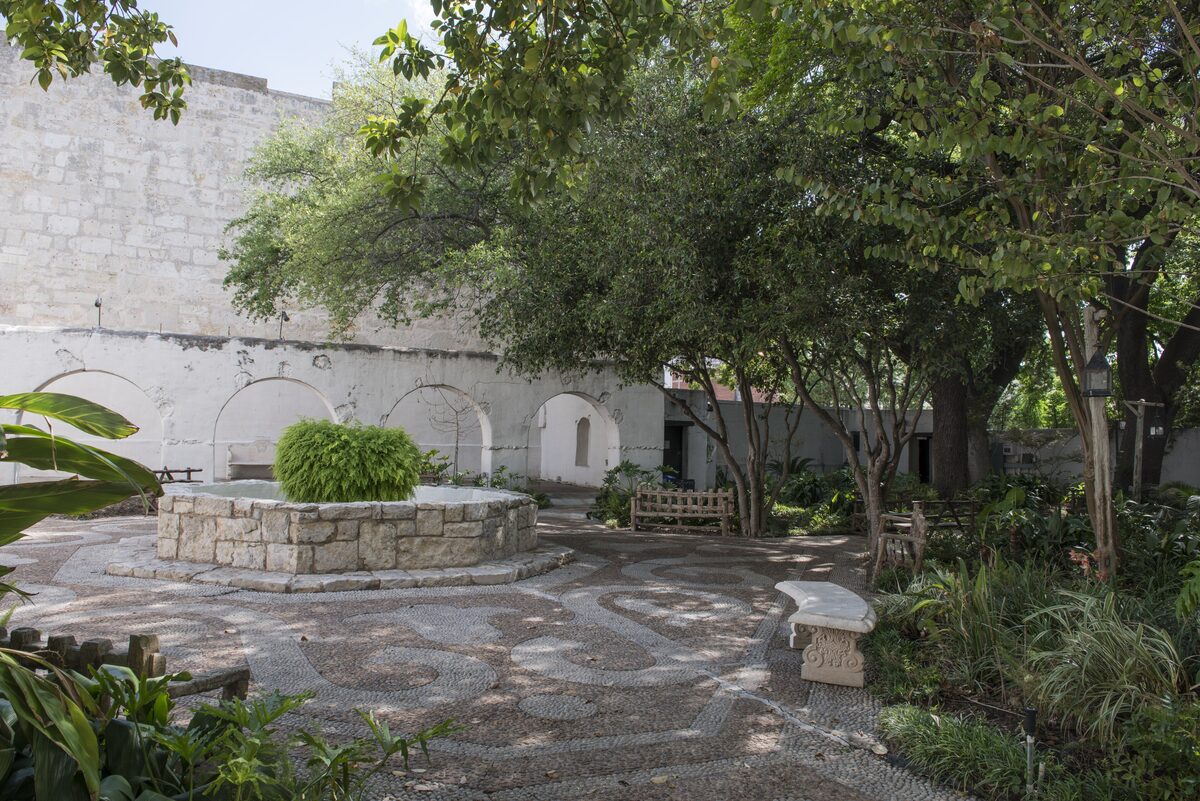 The shaded garden courtyard of the Spanish Governor's Palace with a stone well, benches and whitewashed arches