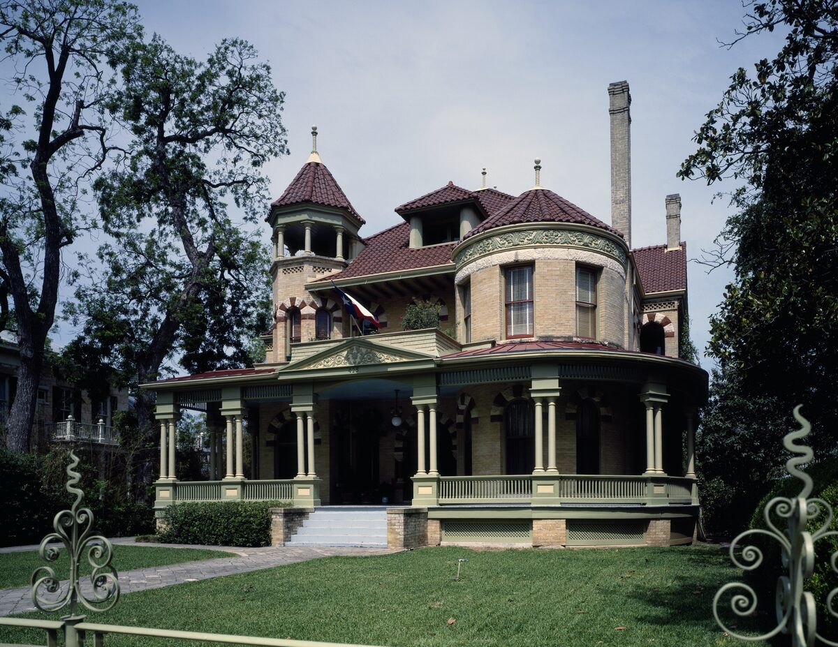 A Victorian mansion with a red-roofed corner tower and wraparound porch in the King William district