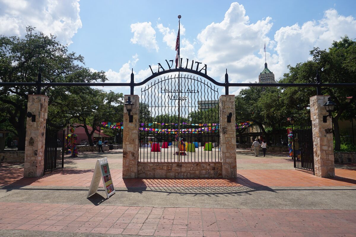 The wrought-iron La Villita entrance gate between stone pillars, with paper flags strung across the brick plaza
