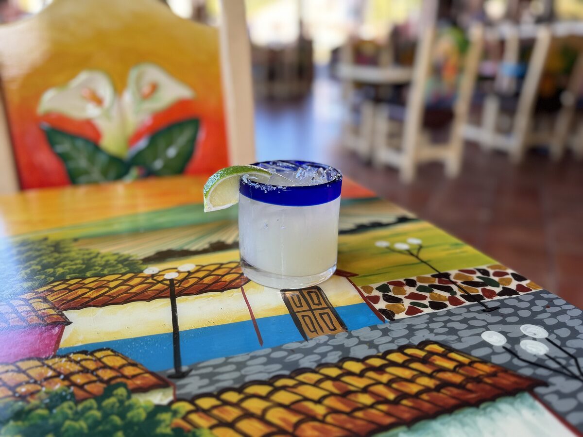 A margarita in a blue-rimmed glass with a lime wedge on a painted table