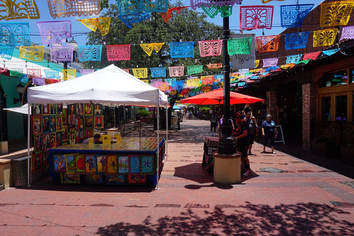 Market Square stalls under strings of colorful papel picado flags and shade trees