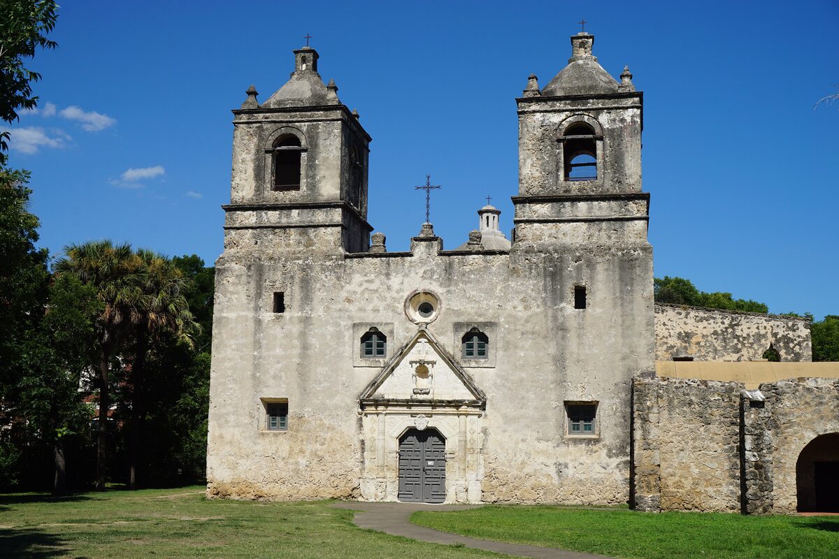 The twin bell towers and stone facade of Mission Concepción rising over a lawn