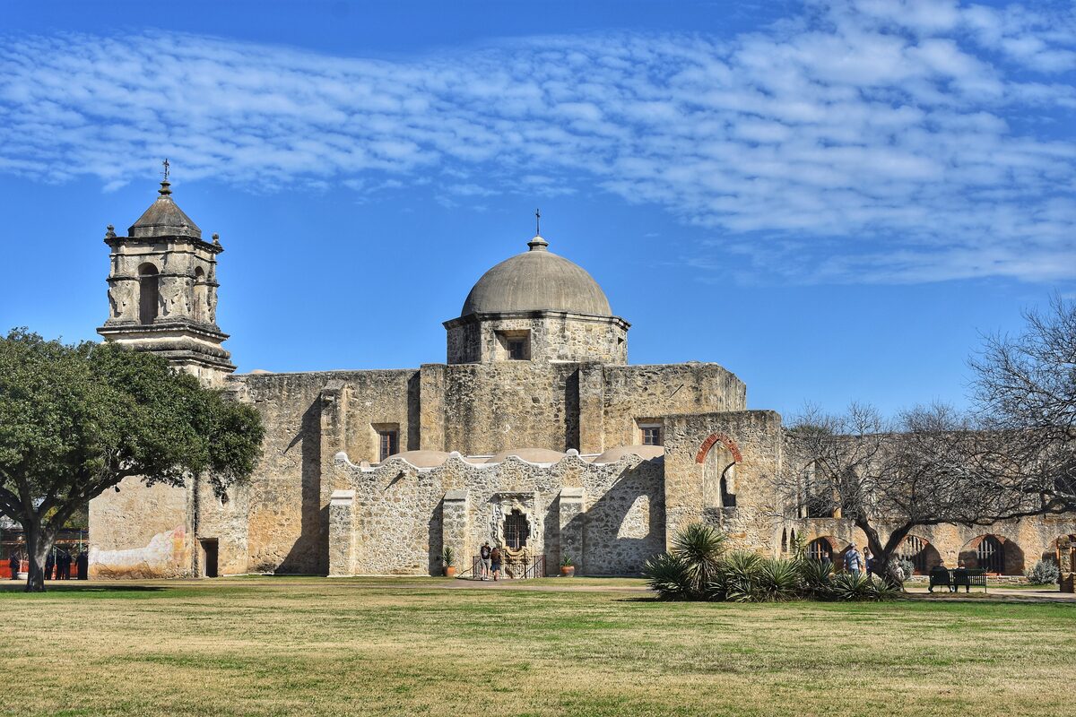 The domed church and arched stone walls of Mission San José seen across the grass