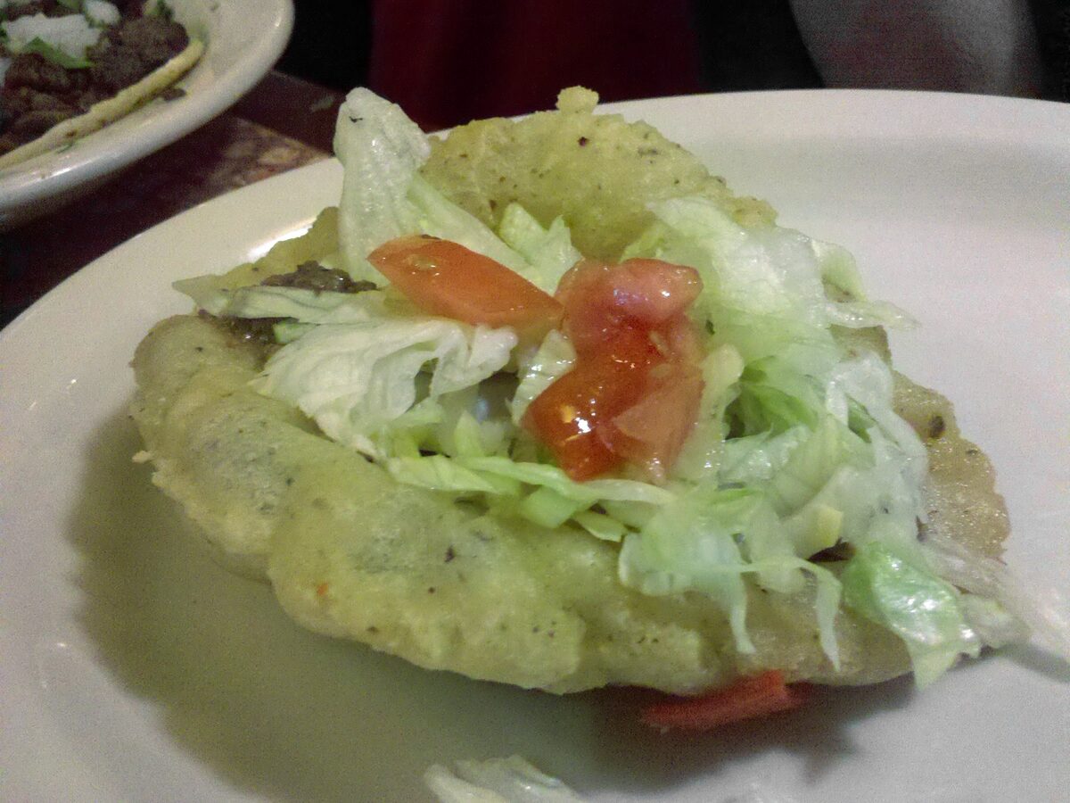 A puffy taco, a fried masa shell filled with lettuce and tomato