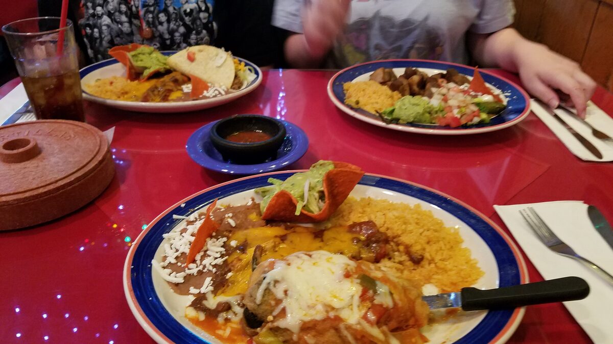 Plates of cheese enchiladas with rice and refried beans on a red table at Mi Tierra