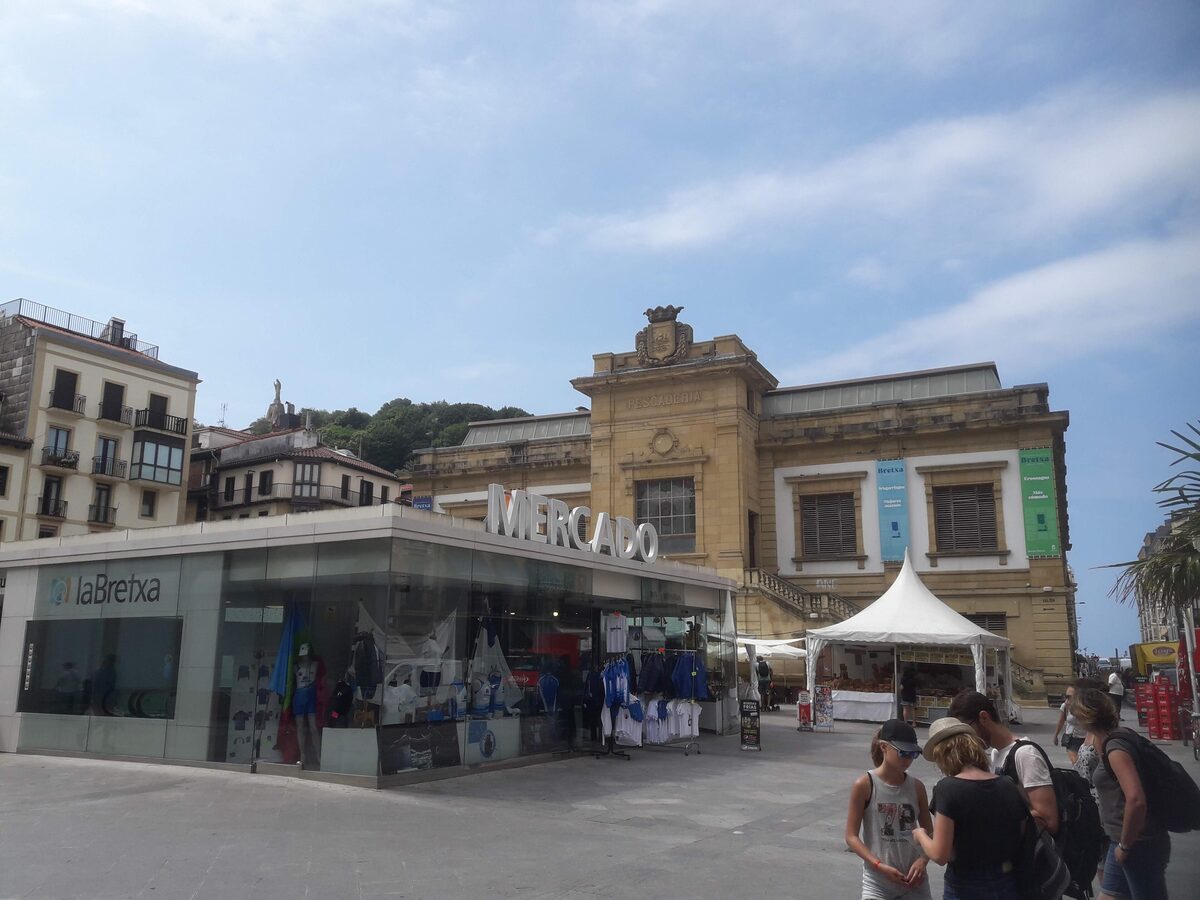 The front of the La Bretxa market hall, with a glass shop front, a Mercado sign on the stone facade and people walking past