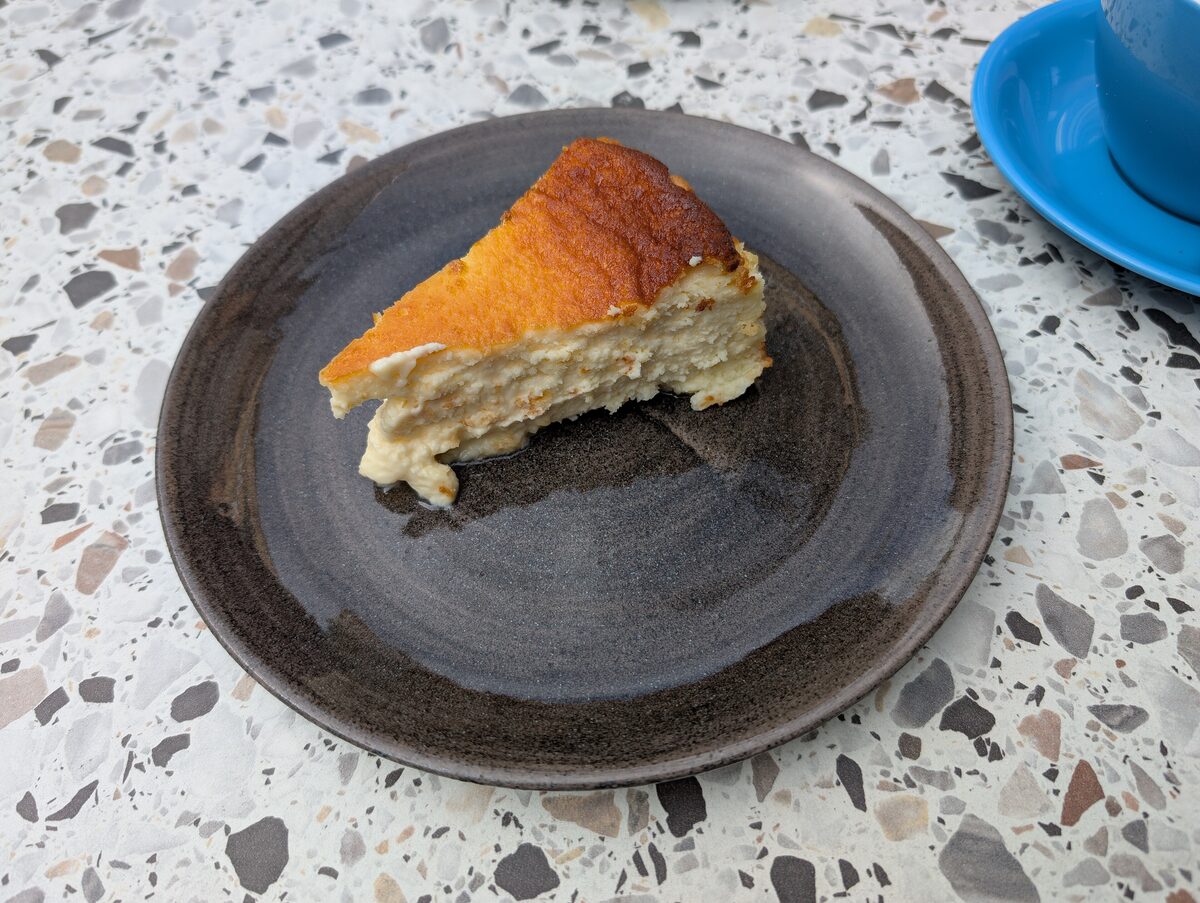 A slice of Basque cheesecake on a dark plate, the top burnt a deep brown and the inside pale and creamy