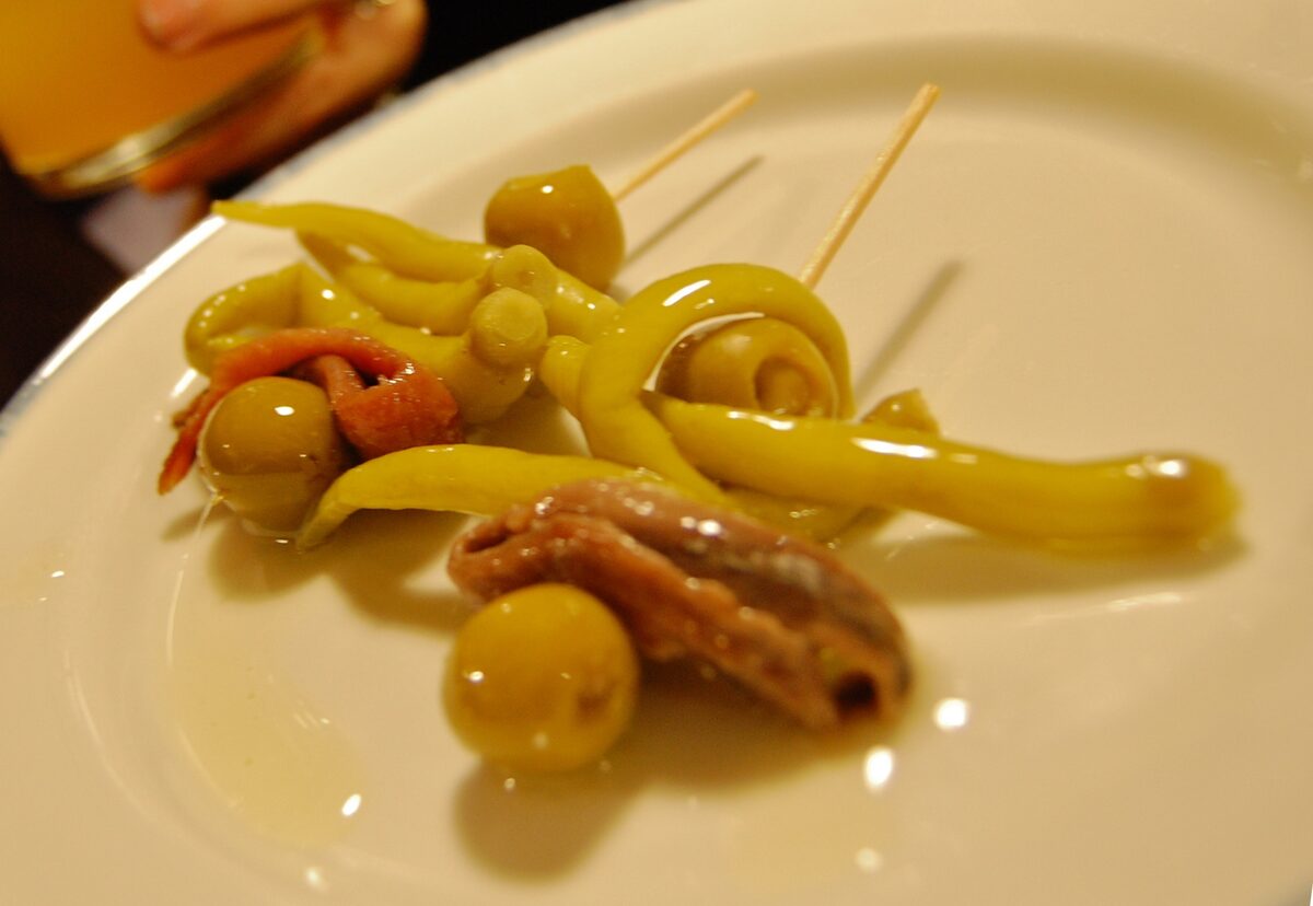 A gilda on a white plate: olives, pickled peppers and an anchovy on a toothpick
