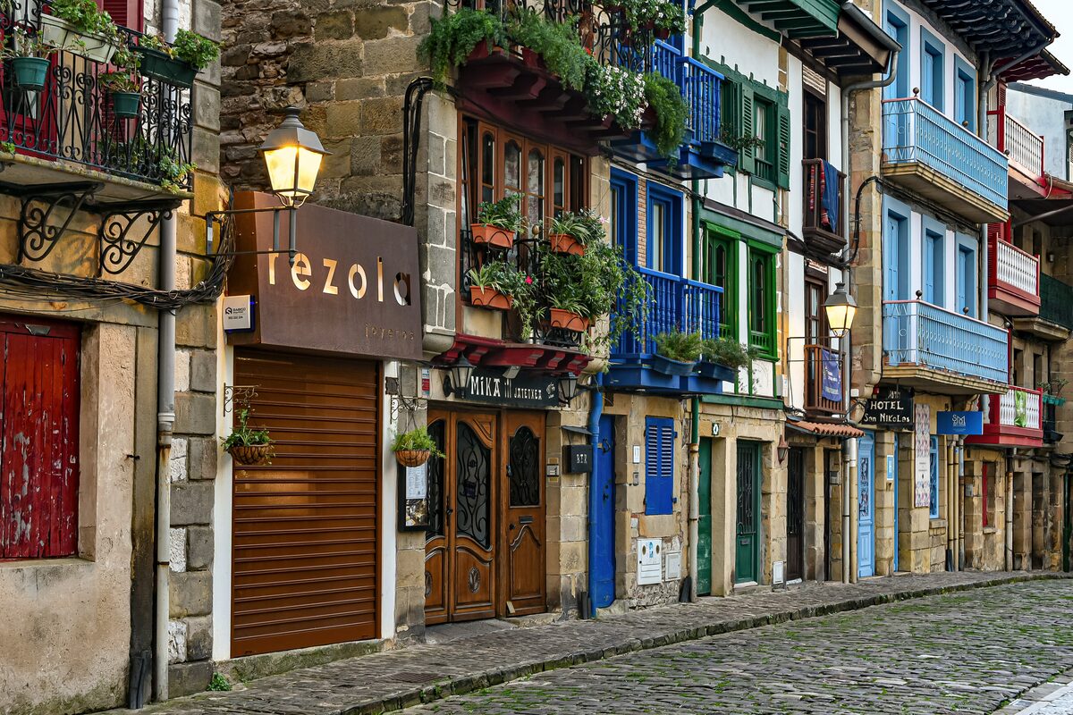 A cobbled street in Hondarribia lined with houses whose wooden balconies are painted blue, green and red, with an iron street lamp