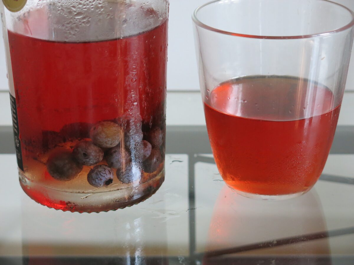 A jar of sloes steeping in red liqueur beside a glass of the finished patxaran