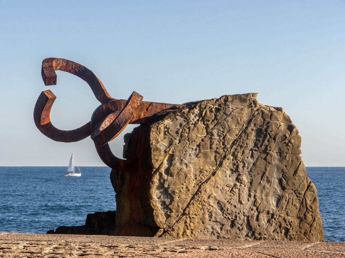 Chillida's Peine del Viento: rusted steel forms set into the rock at the end of the promenade, with the open sea and a sailboat behind