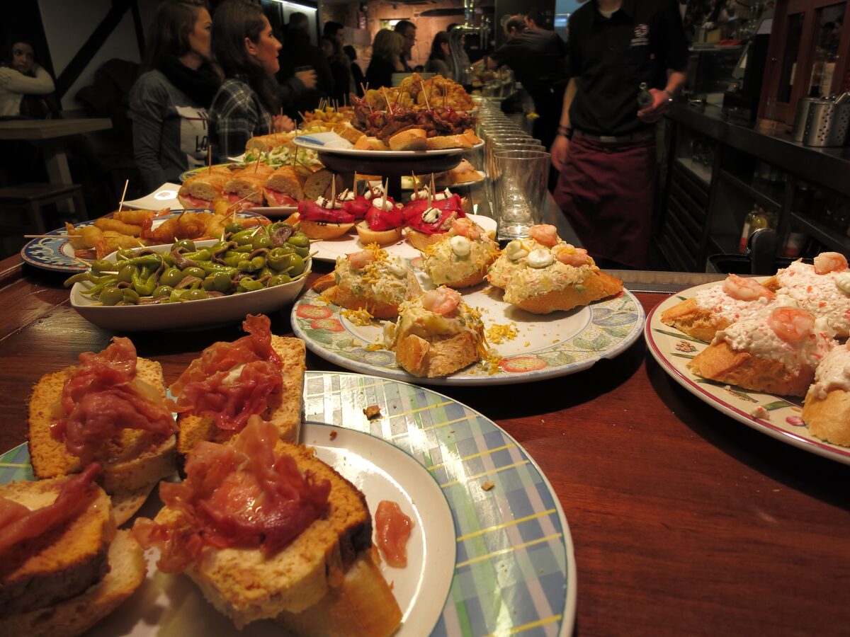 Plates of pintxos on a bar counter: toasts with cured ham, prawns, pickled peppers and more