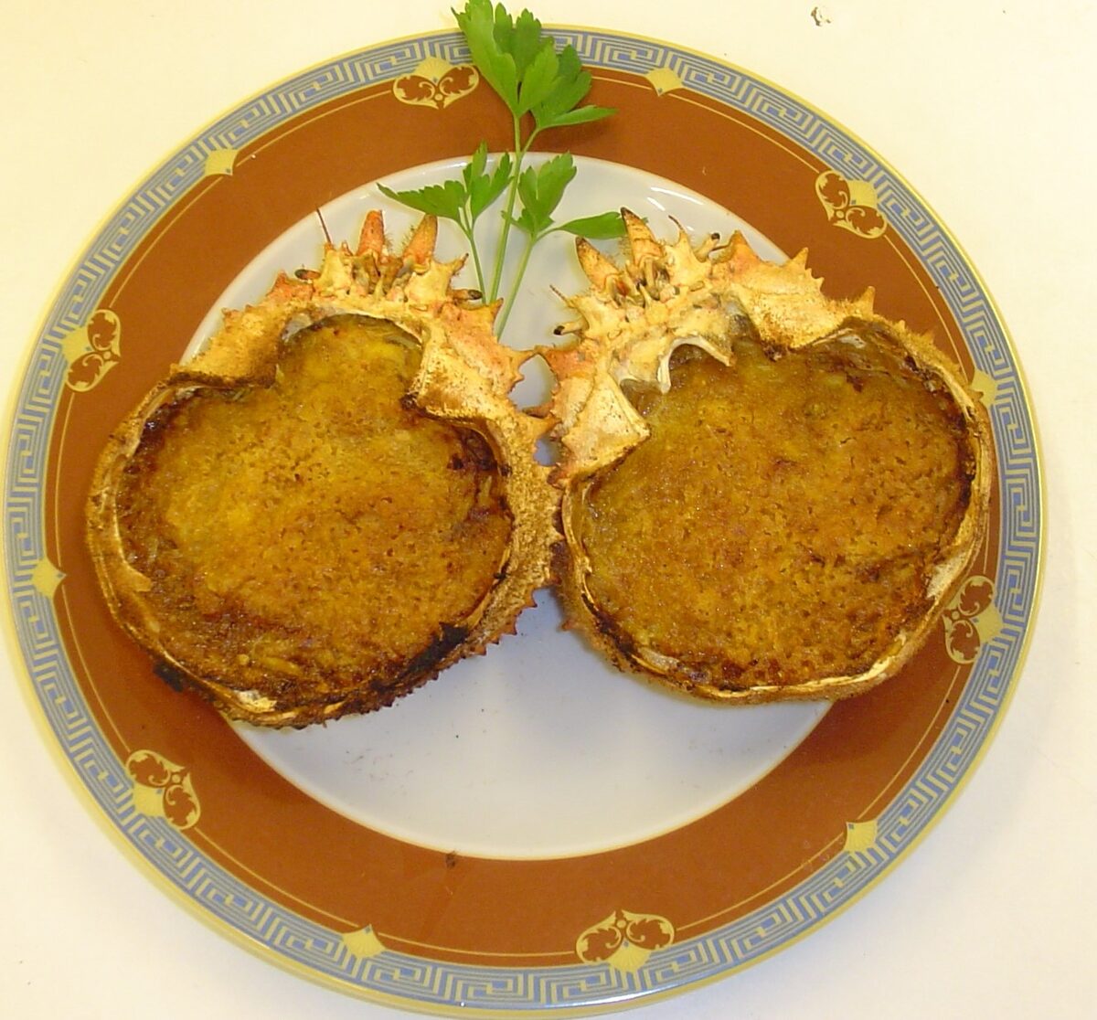 Two spider crab shells filled with baked crab, golden on top, with a sprig of parsley on the plate