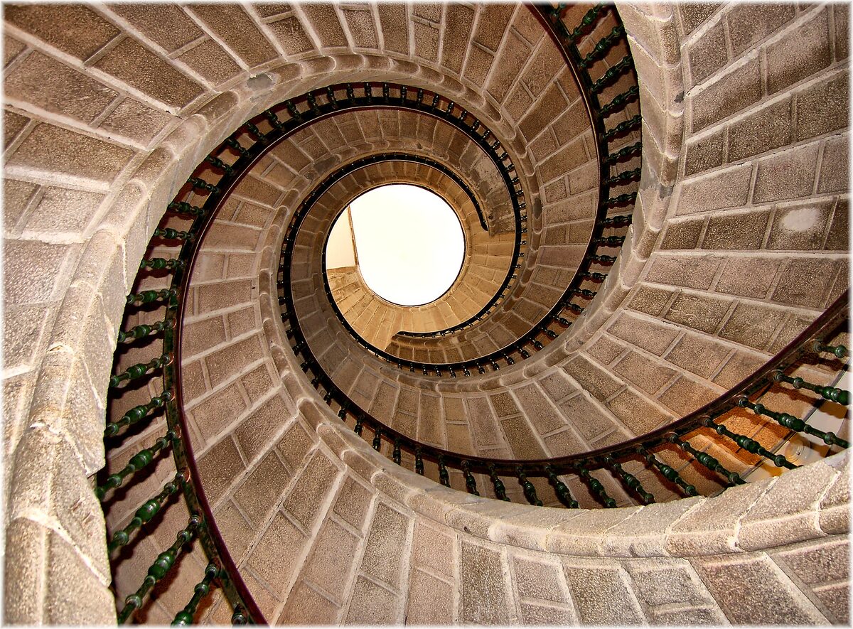 Looking up the triple spiral staircase of the Convent of Bonaval, three stone ramps with iron railings winding around a bright opening