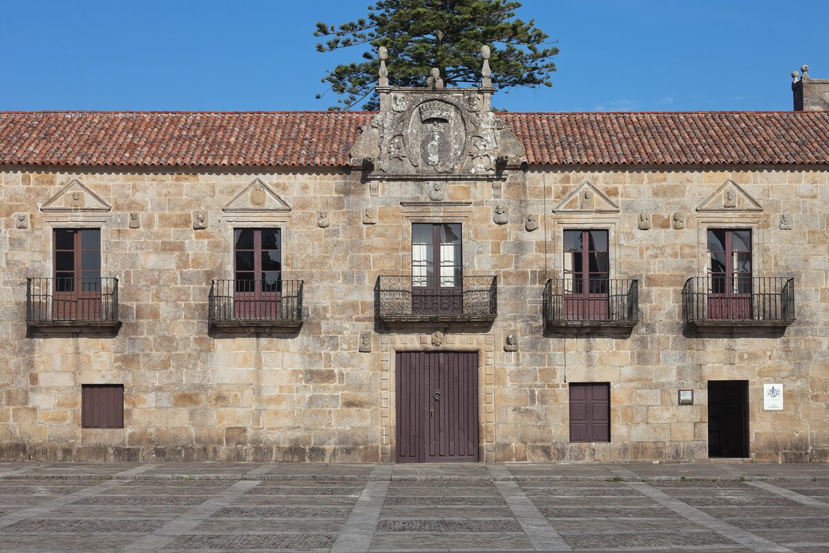 The granite facade of the Pazo de Fefiñáns in Cambados, with a carved coat of arms over the door and a pine behind the red-tiled roof