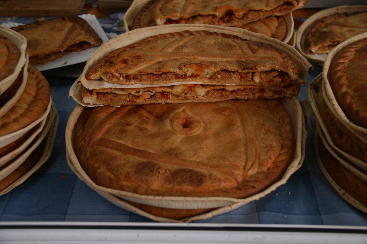 Round Galician empanadas with golden crusts stacked in bakery trays