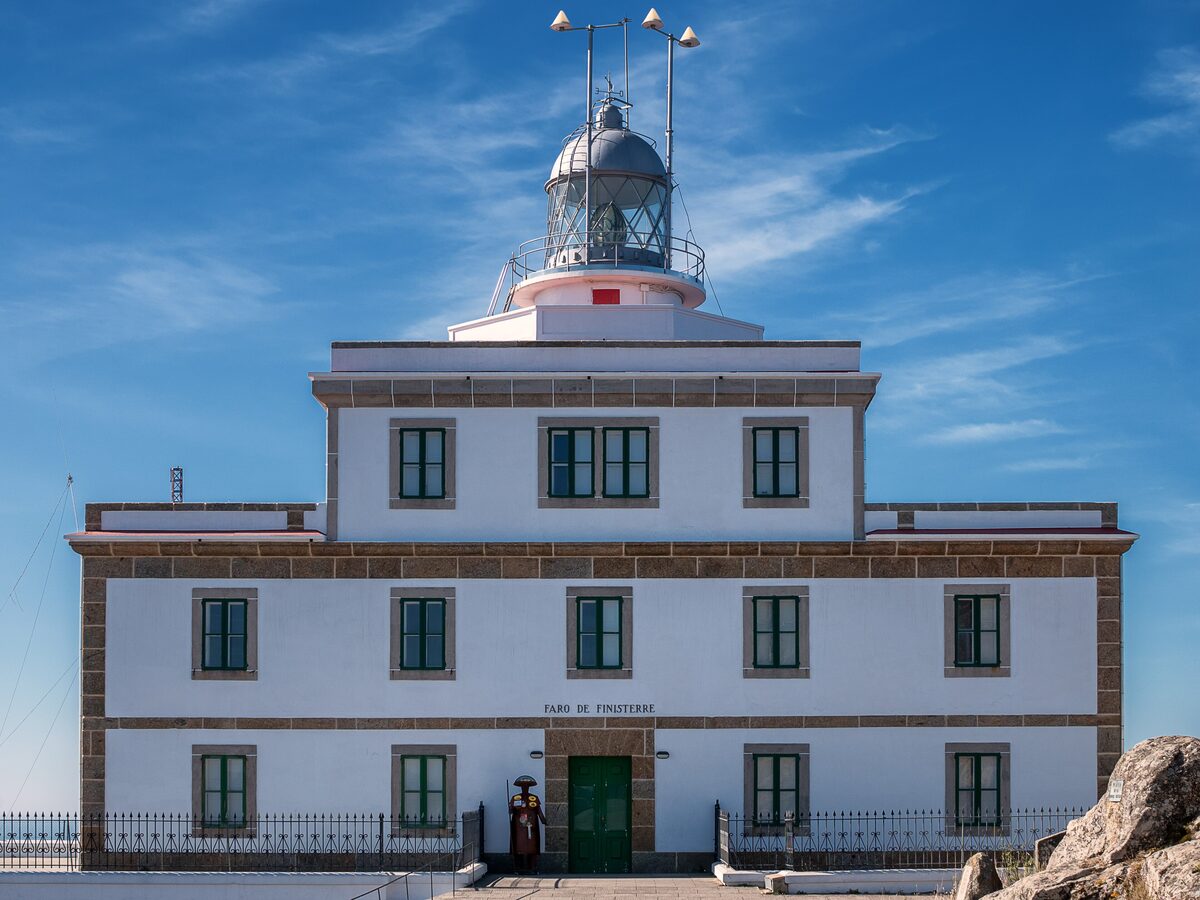 The white lighthouse building at Cabo Fisterra under a clear blue sky, with its lantern tower on top