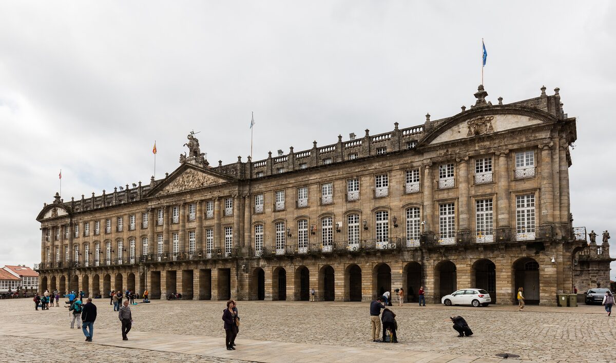 The long neoclassical facade of the Pazo de Raxoi across the Praza do Obradoiro, with a few people on the paving