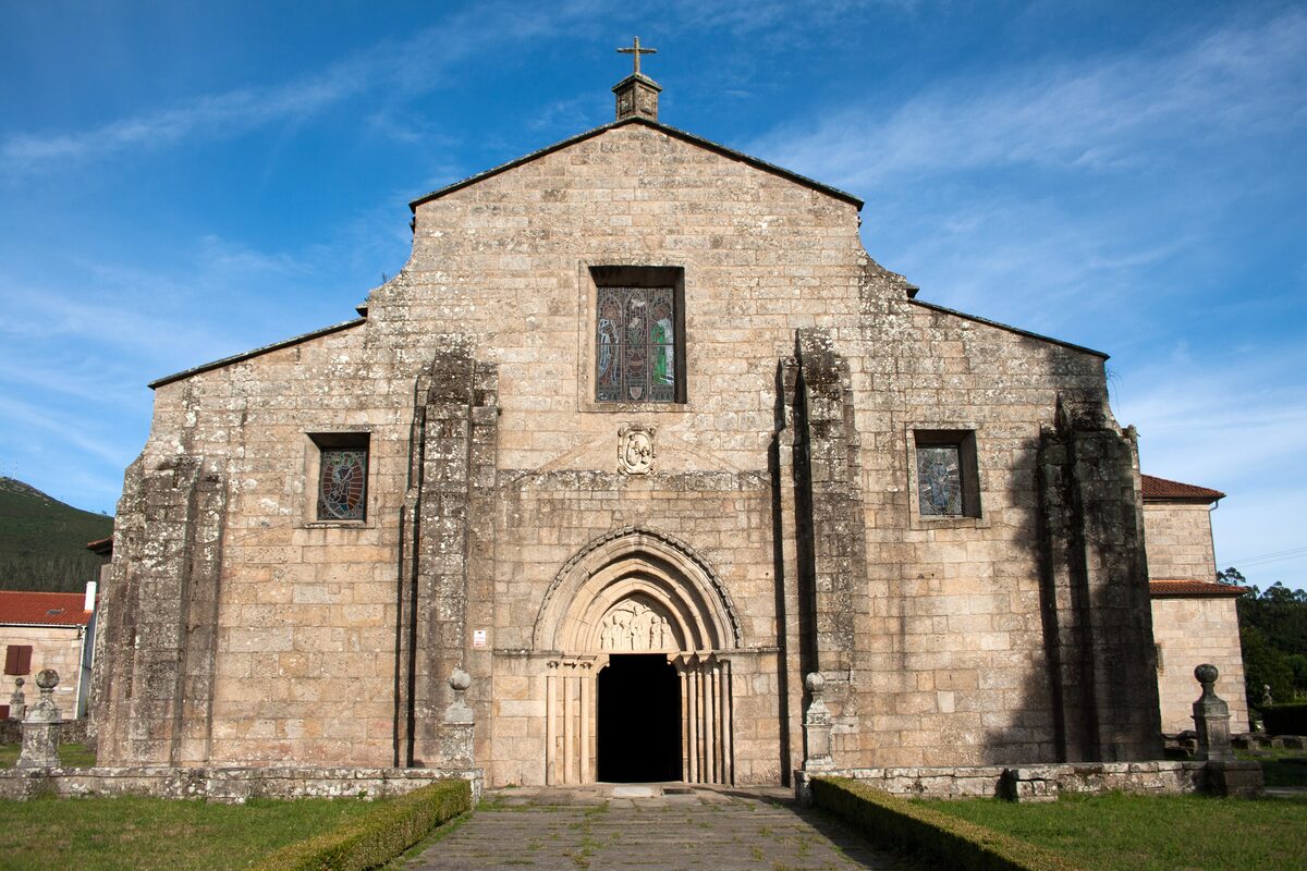The Romanesque stone facade of the Church of Santa María de Iria Flavia under a blue sky