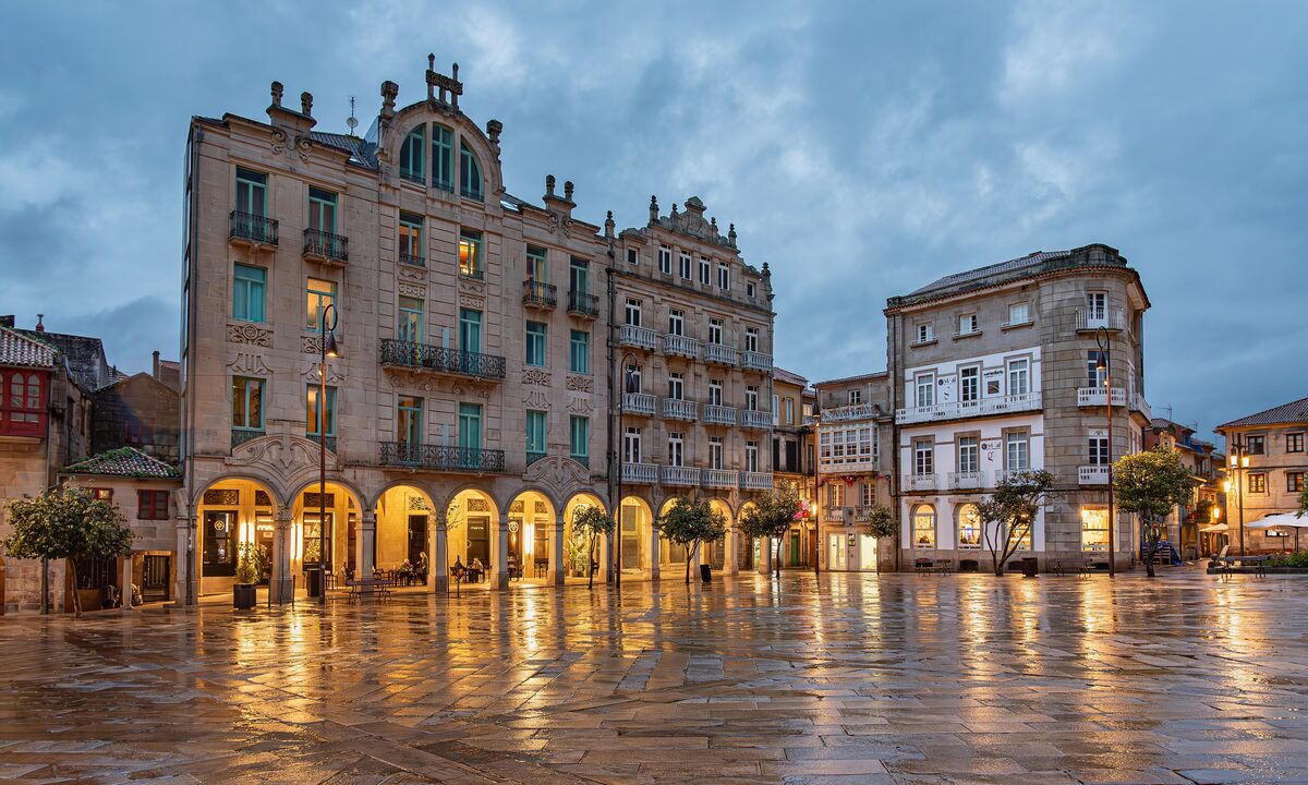 Arcaded old houses on the Praza da Ferraría in Pontevedra, with the wet paving reflecting the evening lights