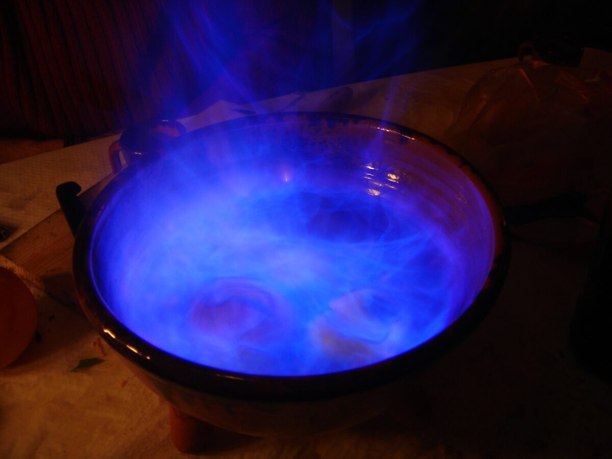 A clay bowl of queimada with the blue flame of burning orujo in a dimly lit room