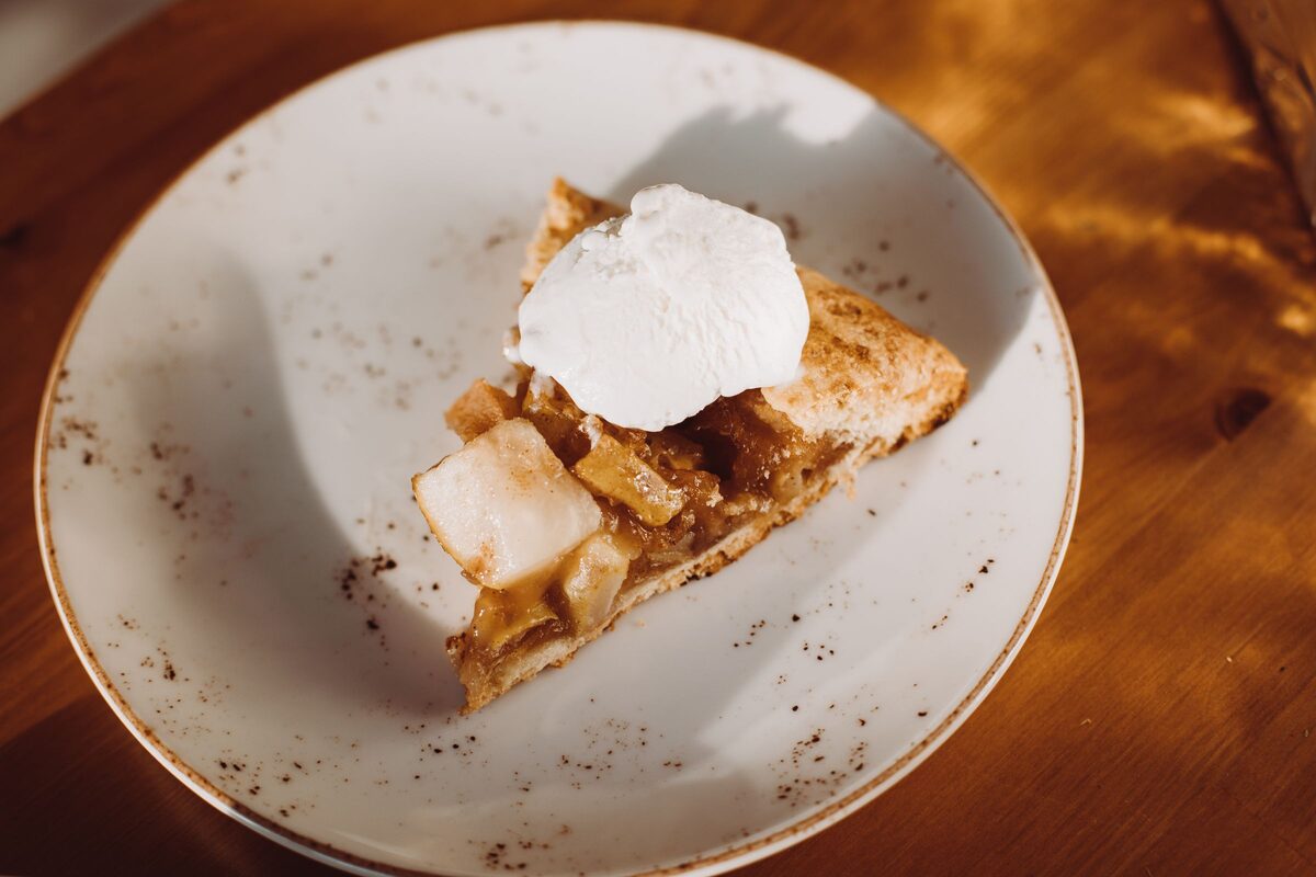 Slice of apple pie topped with whipped cream on a plate