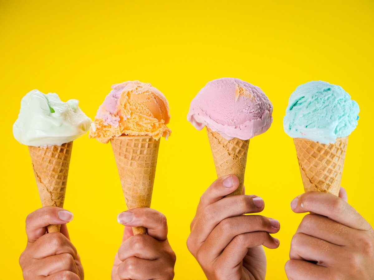 Four hands holding ice cream cones against a yellow backdrop