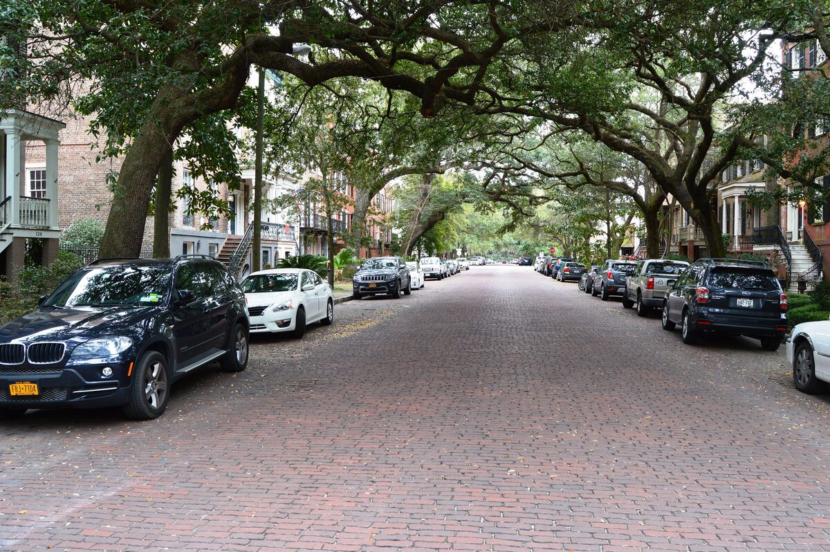 Brick-paved Jones Street lined with parked cars under live oaks