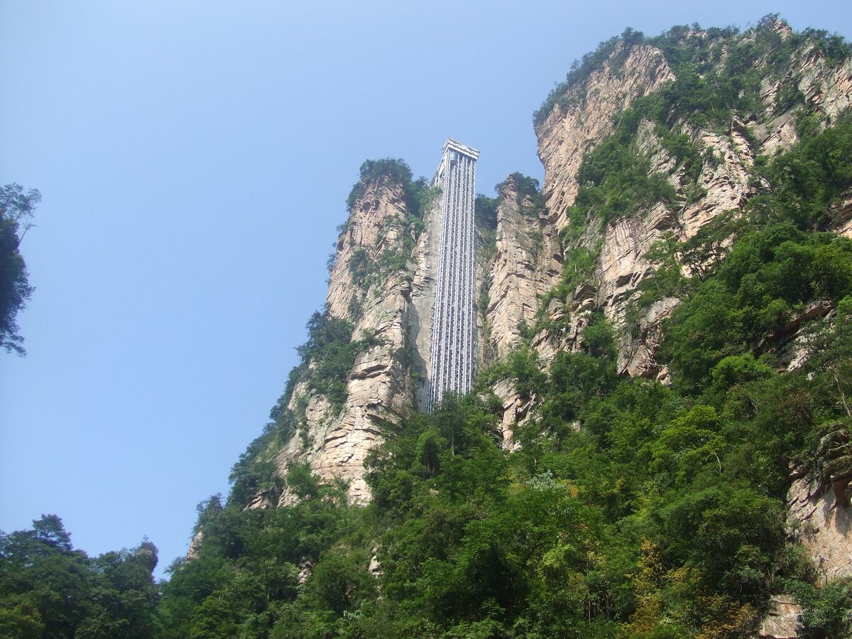 The Bailong Elevator, a glass-and-steel tower running up a sandstone cliff face under a clear blue sky