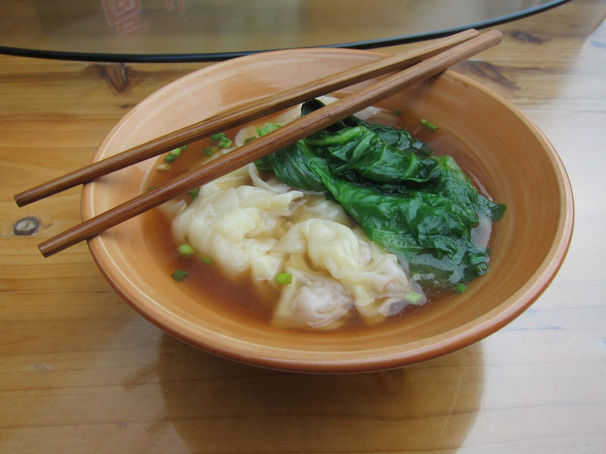 A wooden bowl of wonton soup with spinach and chopsticks, eaten in Wulingyuan