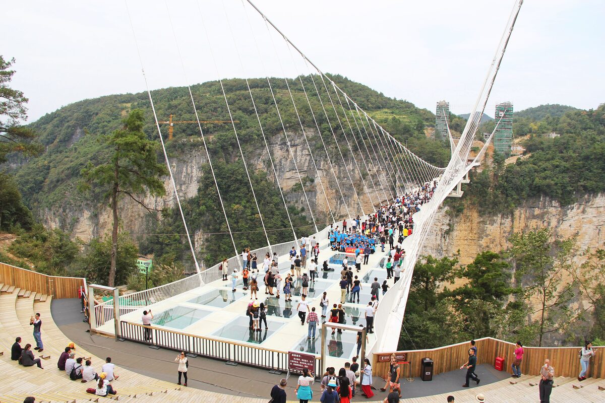 The Zhangjiajie Grand Canyon glass bridge stretching across a forested canyon on suspension cables, with visitors on the deck