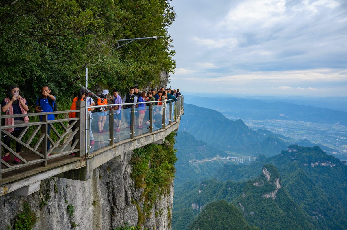 Visitors on the glass-floored cliffside walkway at Tianmen Mountain, with forested ridges and a valley far below