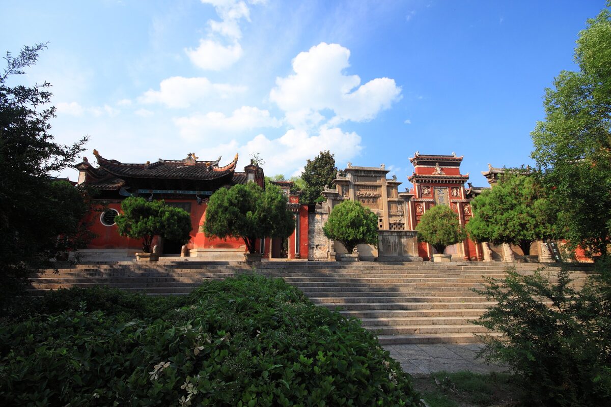 Red-walled halls of Puguang Chan Temple behind a stone terrace and trimmed trees under a blue sky