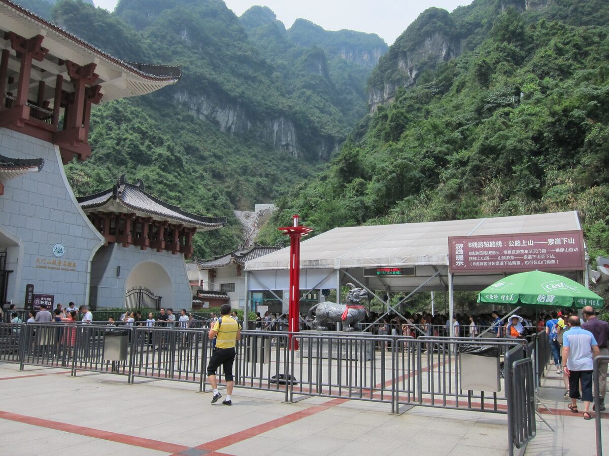 Queue barriers and tiled-roof buildings at the foot of Tianmen Mountain, with steep green cliffs behind